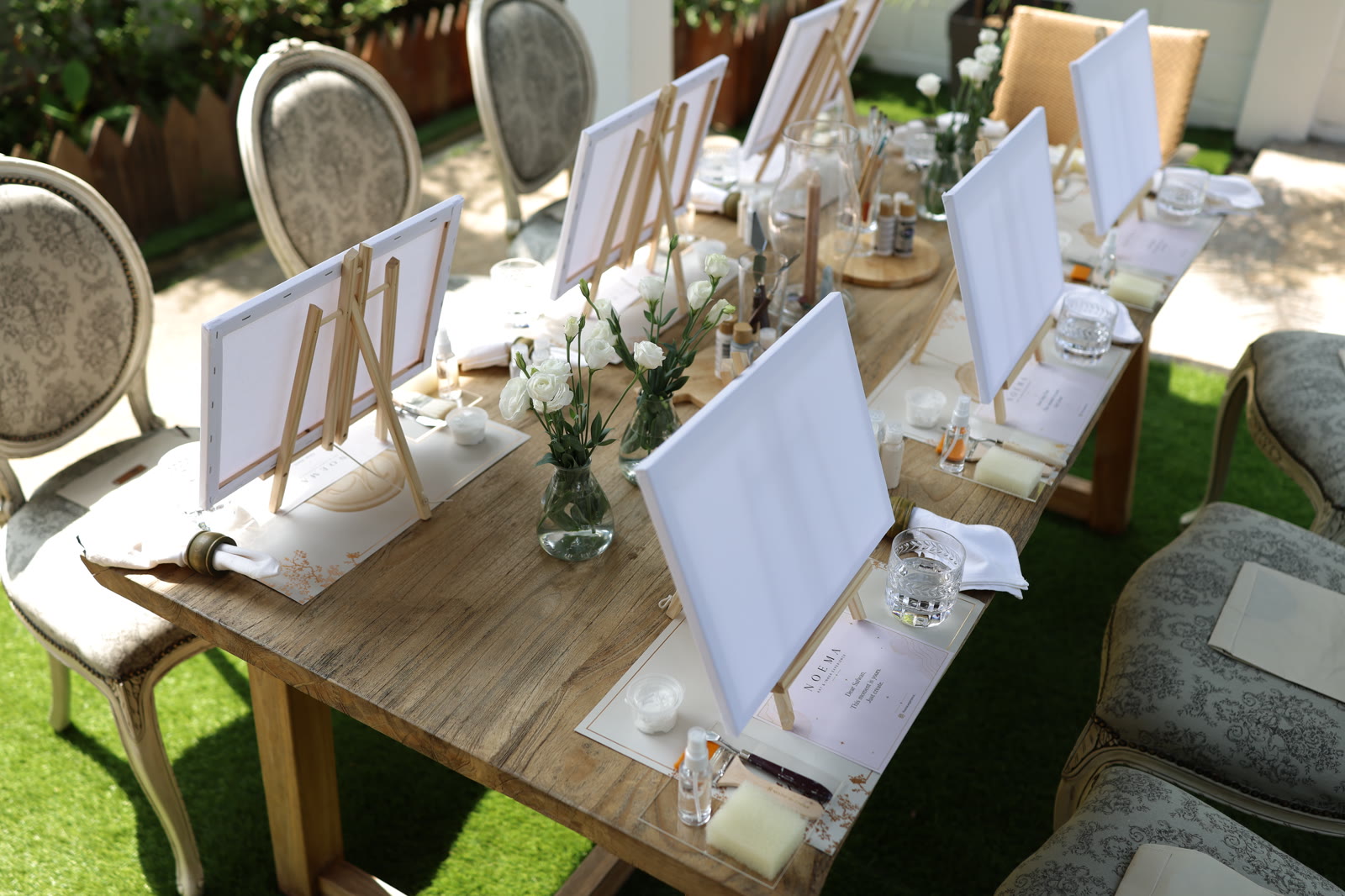 The prepared table before guests arrive — eight canvases on easels, white flowers
